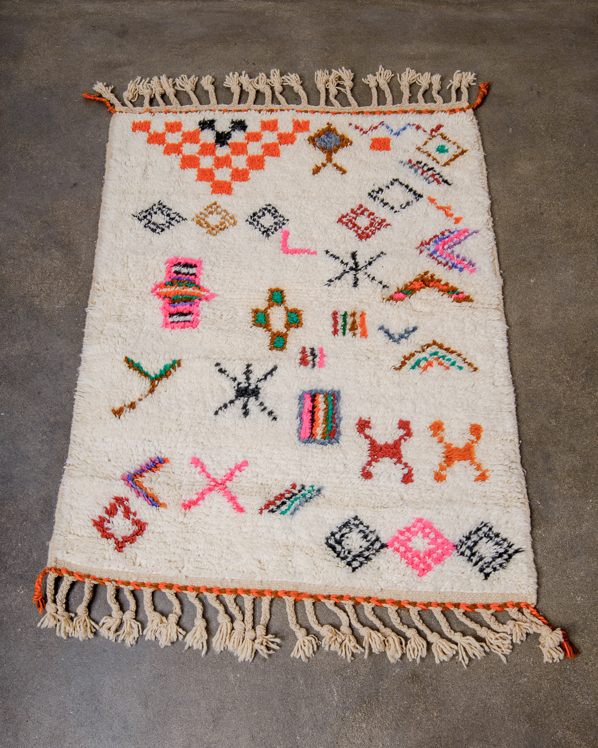 Berberlin special edition Beni Ourain rug made of cream wool with abstract design details featuring orange, brown and neon pink laying on concrete floor.